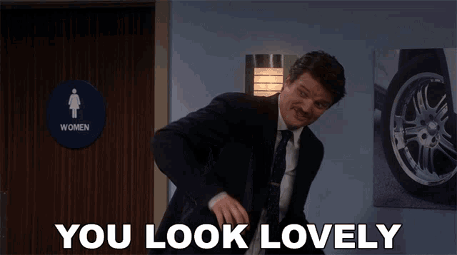 a man in a suit and tie stands in front of a women 's bathroom