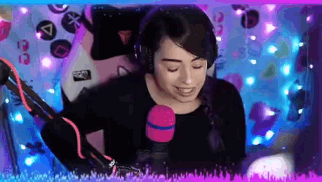 a woman wearing headphones and a pink microphone is smiling in front of a video game controller .