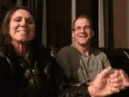a man and a woman are clapping while sitting on a couch .