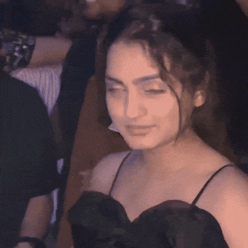 a woman in a black dress is giving the middle finger while sitting in a crowd of people .
