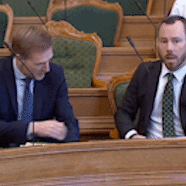 two men in suits and ties are sitting in front of microphones in a room