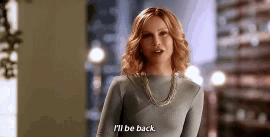 a woman in a blue dress is standing in a room and says `` i 'll be back '' .