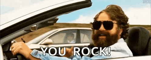 a man with a beard and sunglasses is driving a car and says you rock !