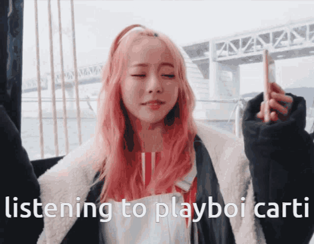 a woman with pink hair is listening to playboy carti