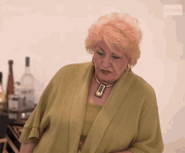 an older woman wearing a green sweater and a gold necklace is standing in front of a table .