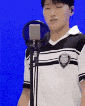 a young man is singing into a microphone while wearing a black and white striped shirt .