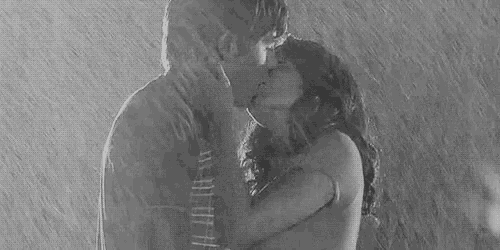 a black and white photo of a man and a woman kissing in the rain .