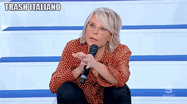 a woman in a red polka dot shirt holds a microphone and says trash italiano on the bottom