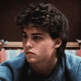 a young man with curly hair wearing a blue sweater
