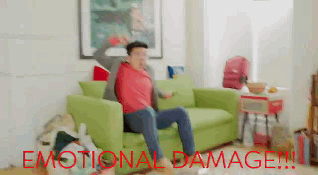 a man is sitting on a green couch with emotional damage written in red
