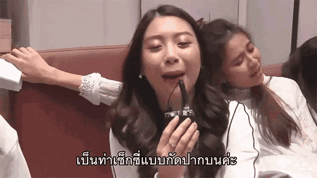 two women are sitting on a couch and one is holding a microphone in her mouth .