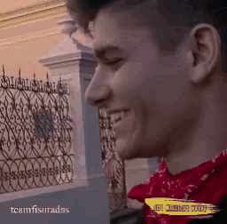 a man in a red shirt is smiling in front of a wrought iron fence with the words los caminos muertos on it