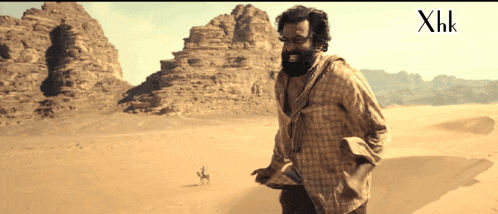 a man in a plaid shirt is standing in a desert with xhk written in the corner