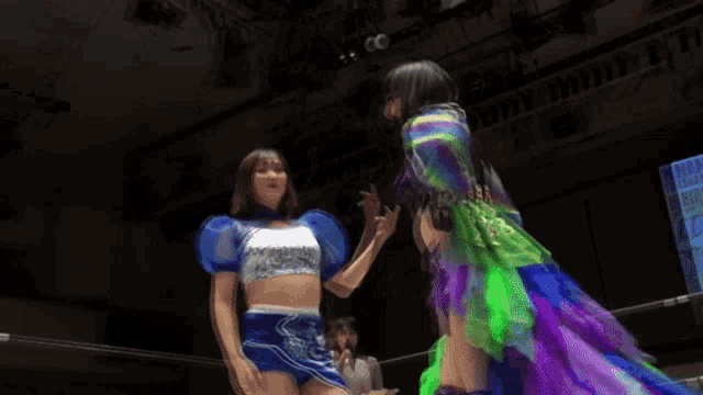 two women wrestling in a ring with one wearing a purple and green dress
