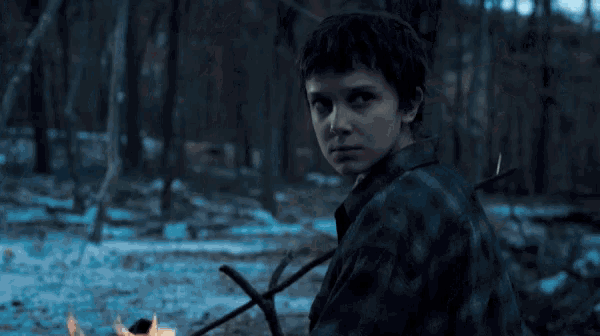 a close up of a person 's face in a dark forest with a fire in the background .