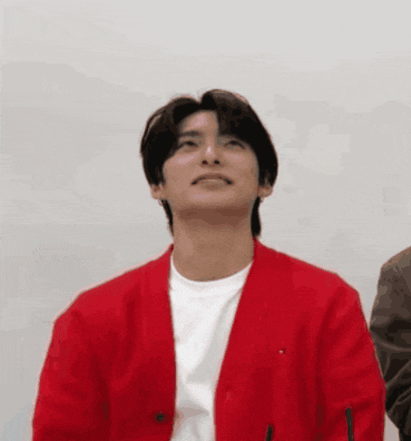 a young man wearing a red cardigan and a white t-shirt is looking up .