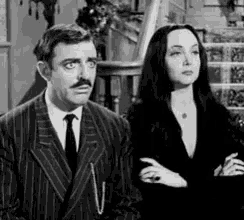a man in a suit and tie and a woman in a black dress are standing next to each other .
