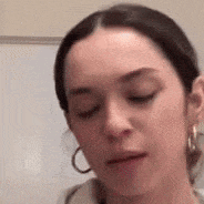 a woman wearing hoop earrings and a hoodie is making a funny face .