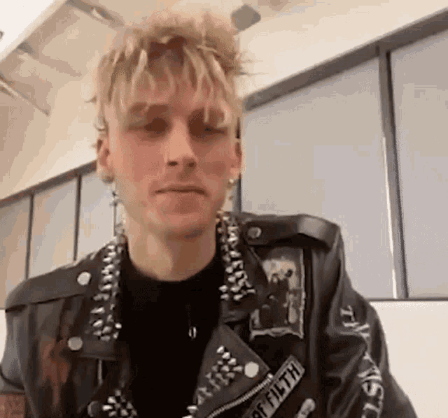 a young man wearing a leather jacket with spikes on it is sitting in a room .