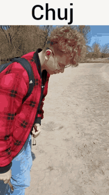 a man in a red plaid shirt is standing in the sand with the word chuj written above him