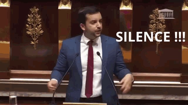 a man in a suit and tie stands at a podium with the word silence written above him