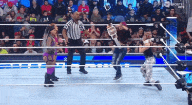 a group of people are wrestling in a ring with a referee standing behind them .