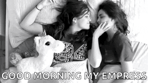 two women are laying in bed with a stuffed unicorn and kissing .