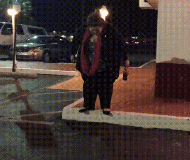 a woman in a red scarf stands in a parking lot at night