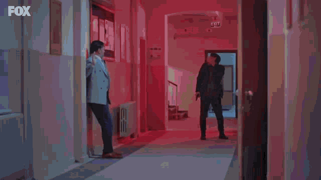 a man in a suit is holding a gun in a hallway with a fox logo in the corner