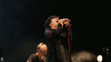 a man sings into a microphone while another man plays guitar