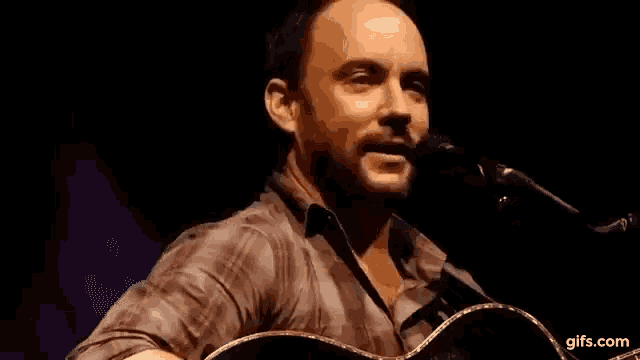 a man is singing into a microphone while holding a guitar in his hand .