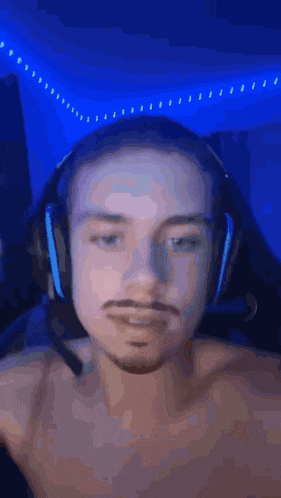 a man without a shirt is wearing headphones with a blue light behind him