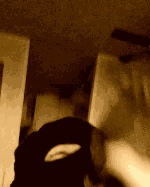 a person wearing a ski mask in a dark room with a ceiling fan in the background