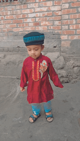 a young boy wearing a red shirt and a black hat is standing in front of a brick wall