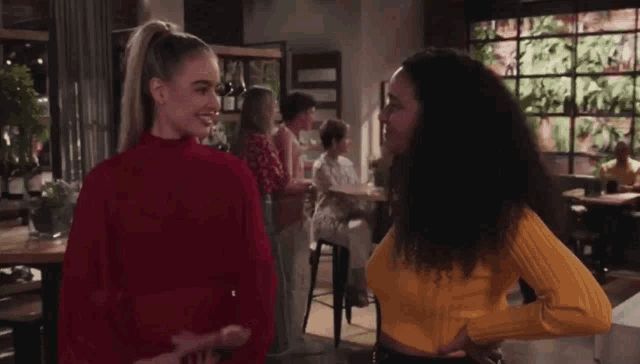 two women are standing next to each other in a restaurant talking to each other