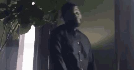 a man in a black shirt and hat is standing in front of a window in a dark room .