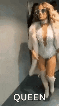 a woman wearing a fur coat and sunglasses is walking down a hallway and saying queen .