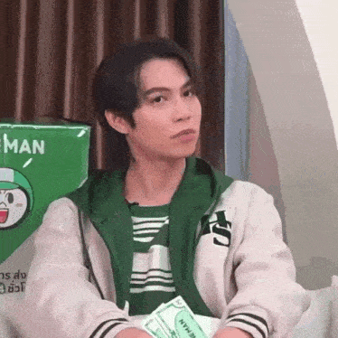 a young man in a green jacket is sitting on a couch holding a packet of money .