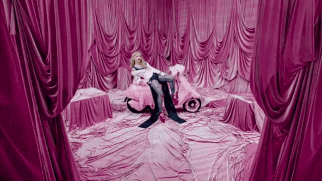 a woman is sitting on a pink scooter in a room covered in pink curtains .