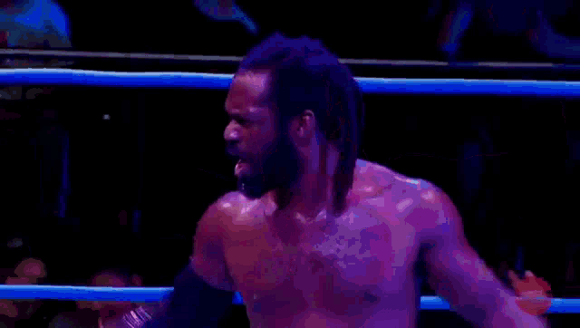 a wrestler is standing in a ring with his tongue out .