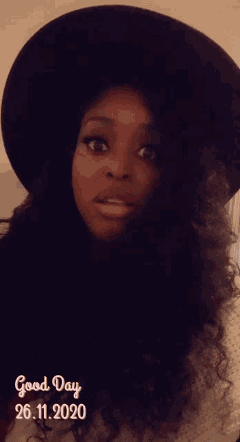 a woman wearing a black hat and a white sweater with the date 26.11.2020