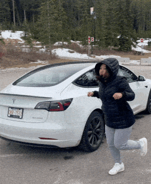 a woman in a black jacket is running towards a white tesla
