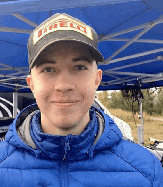 a young man wearing an irelli hat and a blue jacket smiles for the camera