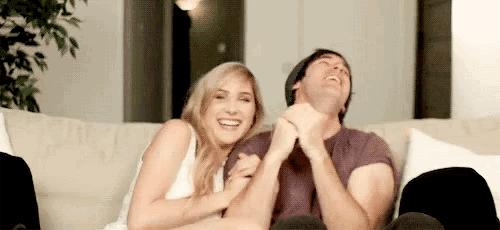 a man and a woman are sitting on a couch laughing and holding hands .