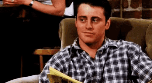 a man in a plaid shirt is sitting in a chair and reading a magazine .