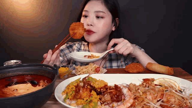 a woman is sitting at a table eating a plate of food with chopsticks