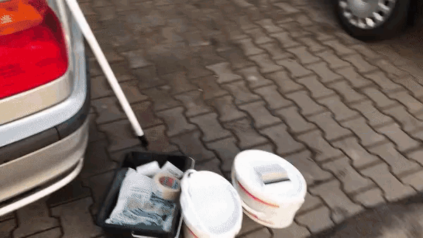 two buckets of paint sit on a brick sidewalk next to a car