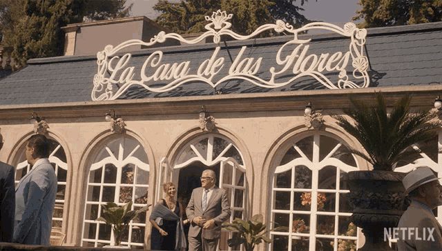 a man in a suit stands in front of a building that says " la casa de las flores "