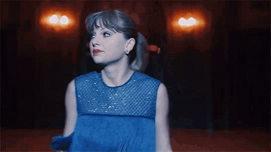 a woman in a blue dress is standing in a dark room looking up .