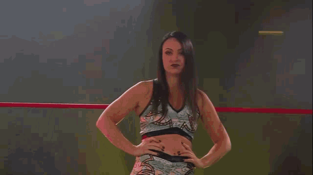 a woman is standing in a ring with her hands on her hips while a referee stands behind her .